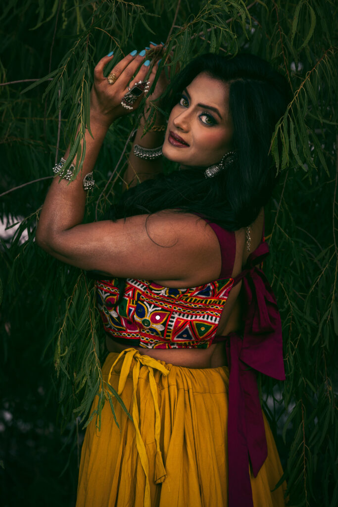 Editorial portrait of Arpita wearing a colorful embroidered top and yellow skirt among green foliage at Brushy Creek Park, Texas.