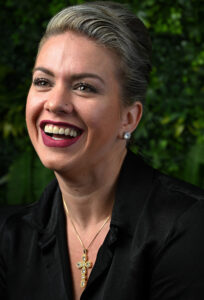 Portrait of hairstylist Leyda Ruiseco smiling against a green foliage background.