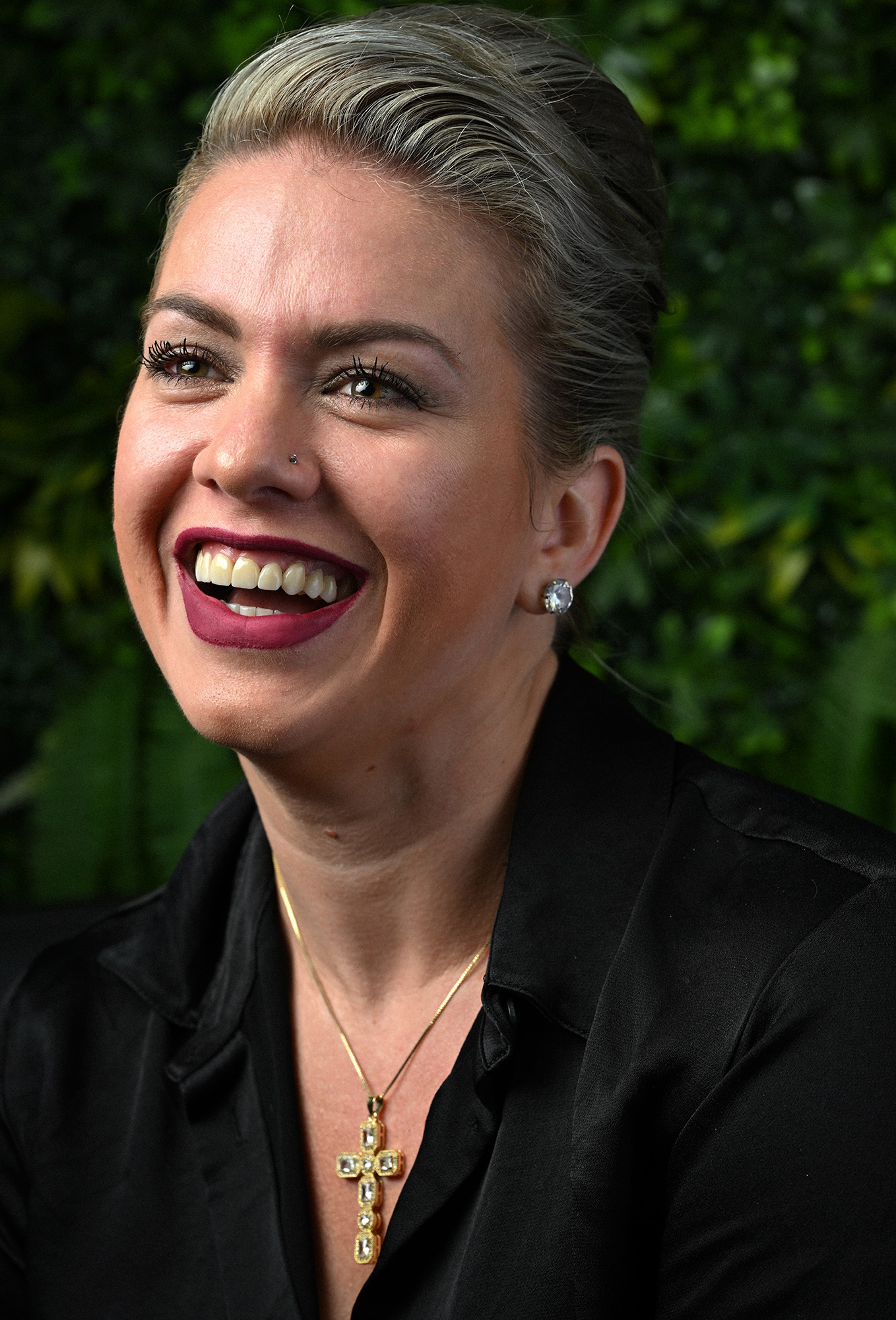 Portrait of hairstylist Leyda Ruiseco smiling against a green foliage background.